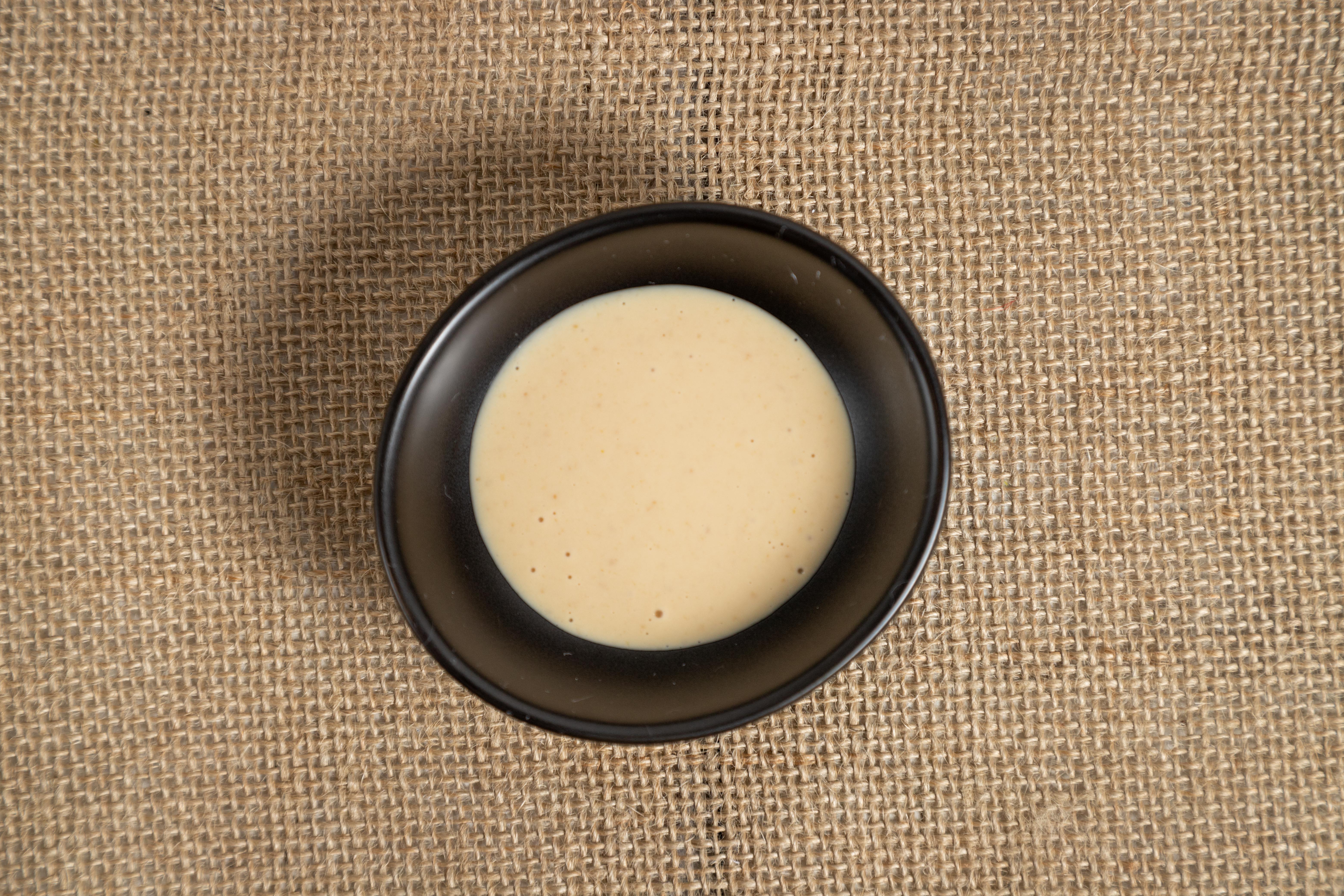 A small black bowl filled with creamy sauce on a textured burlap surface.